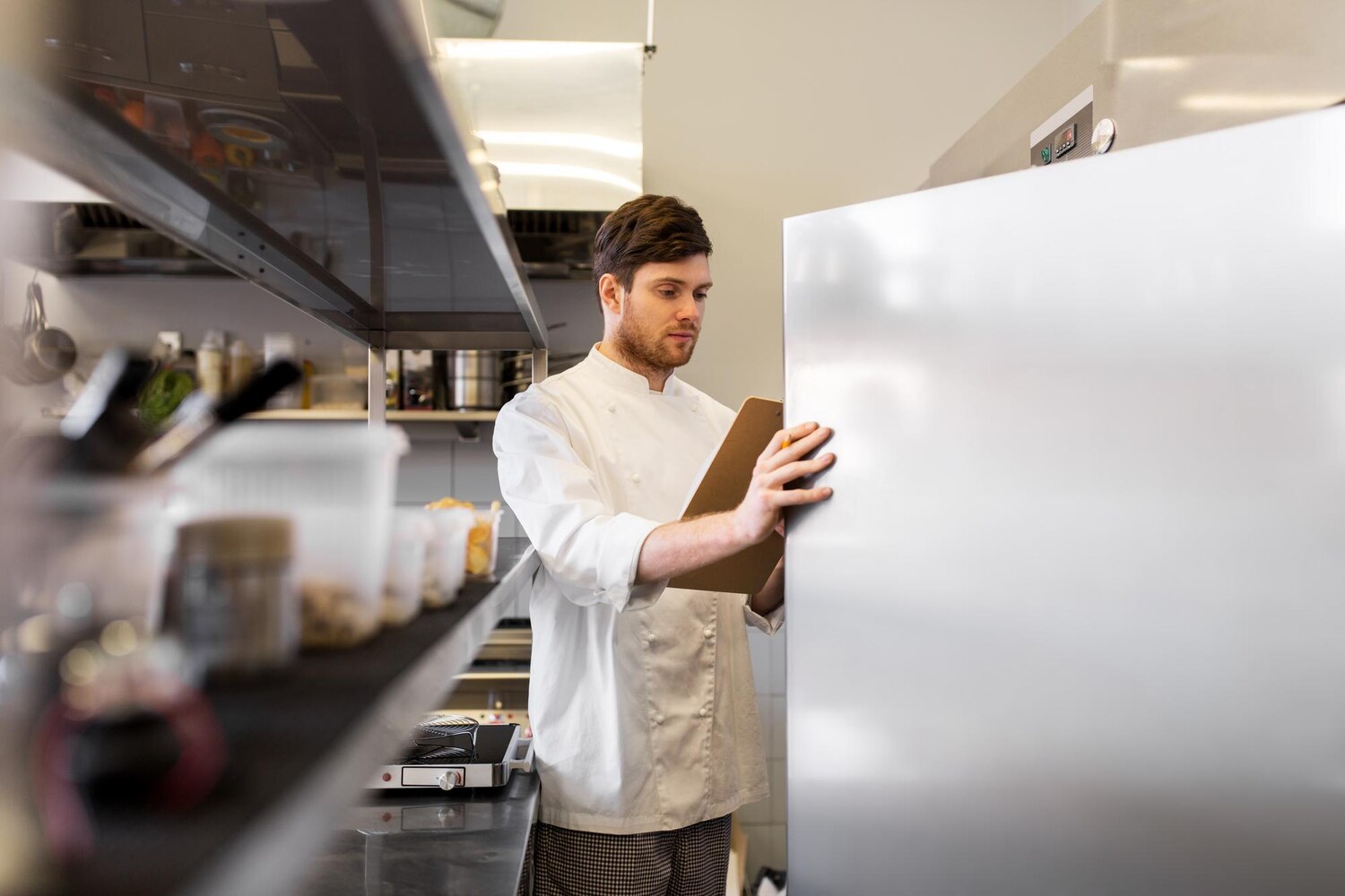 cooking, profession and people concept - male chef cook with clipboard doing inventory in restaurant kitchen fridge